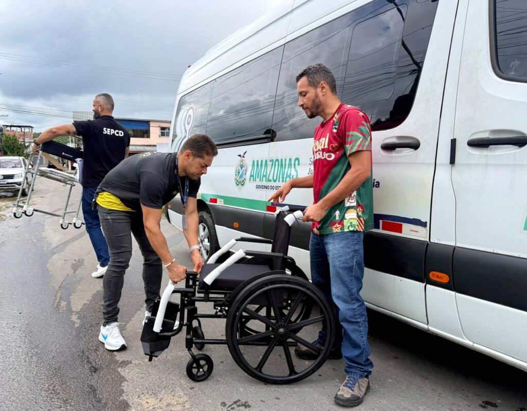 Imagem de servidores montando a cadeira de rodas em frente a van PcD para uma entrega domiciliar