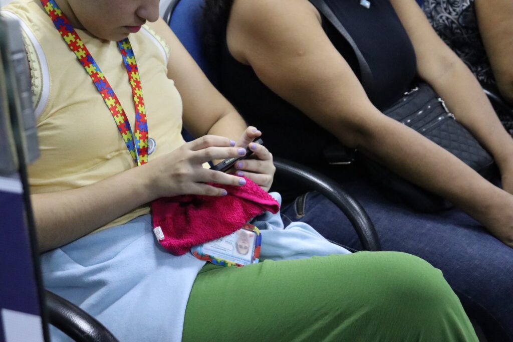 imagem do corpo de uma pessoa sentada mexendo no celular e no seu pescoço o cordão de quebra-cabeças em alusão ao TEA