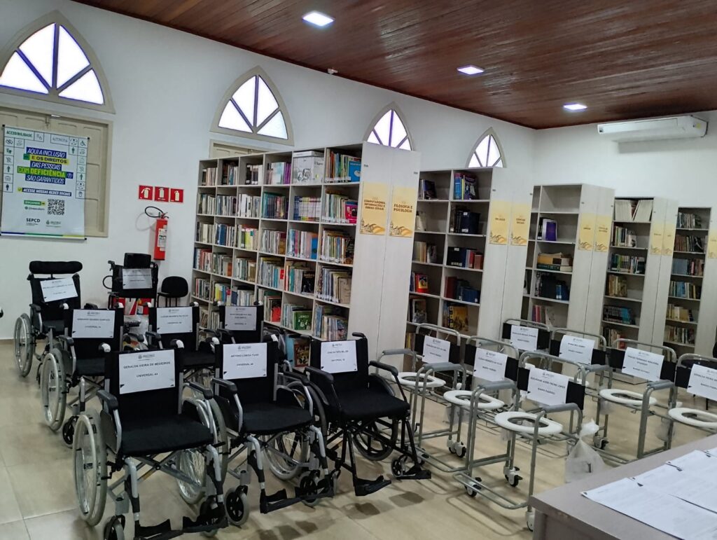 imagem de uma sala, parece uma biblioteca cheia de livros e ao redor várias cadeiras de rodas e de banho ao redor