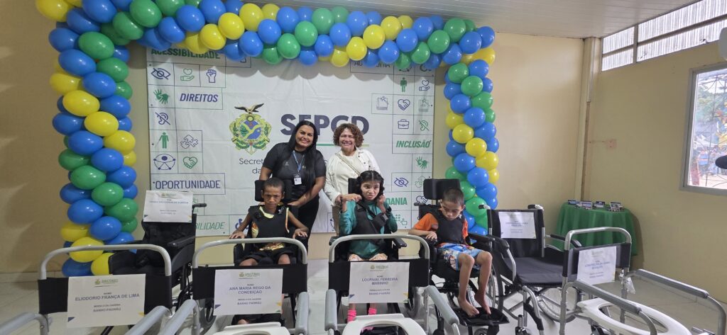 imagem da secretária selma banes e a técnica ao lado sorrindo par a foto junto com várias cadeiras de rodas na frente