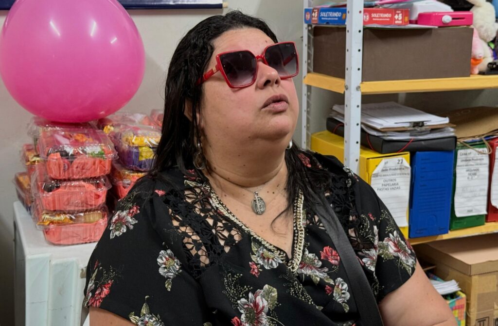cátia usando um vestido preto e um óculos enquanto fala com alguém